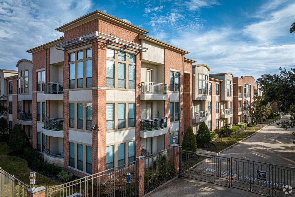 Multi-story brick apartment building with gated entrance under a blue sky.