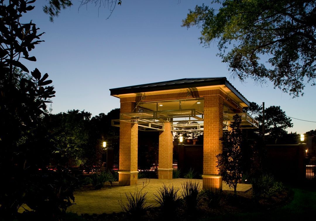 Brick pavilion lit up at dusk, trees frame the edges, blue sky backdrop.