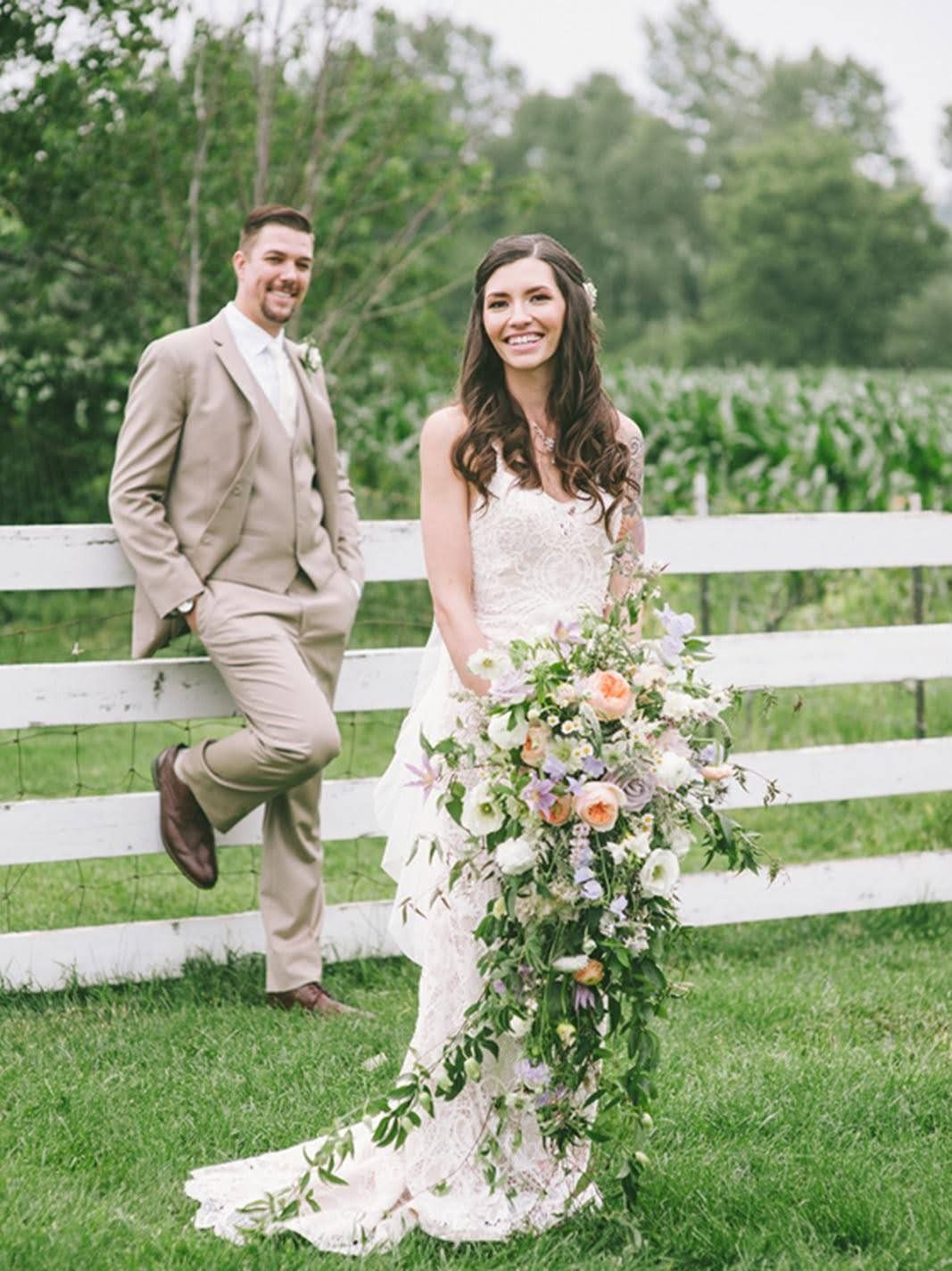 A bride and groom are posing for a picture in front of a white fence.