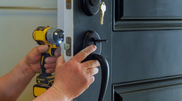 A doors company worker installing a handle in a new front door.  The entry door is a black metal door.