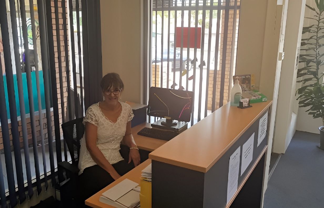 A Woman is Sitting at a Desk in Front of a Computer — Craig Hughes Podiatry in Mount Hutton, NSW