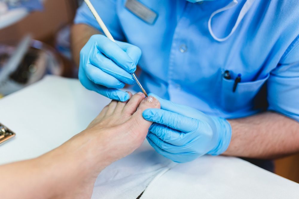 A Man is Painting a Woman's Toenails in a Nail Salon — Craig Hughes Podiatry in Mount Hutton, NSW