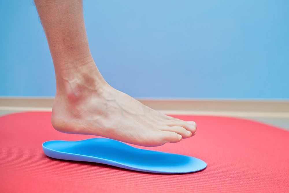 A Person's Foot is Standing on a Red Mat Next to a Blue Insole — Craig Hughes Podiatry in Mount Hutton, NSW