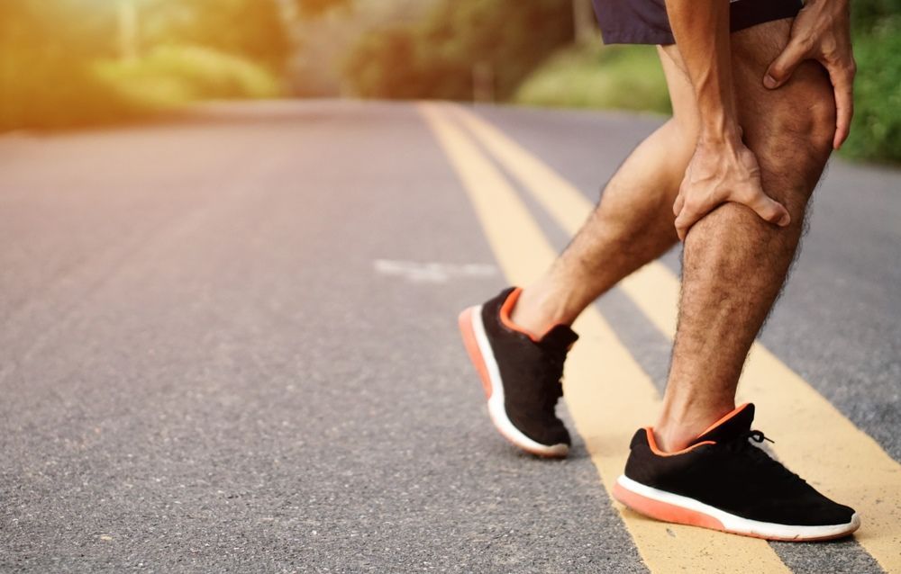 A Man is Holding His Knee in Pain While Walking Down the Road — Craig Hughes Podiatry in Mount Hutton, NSW
