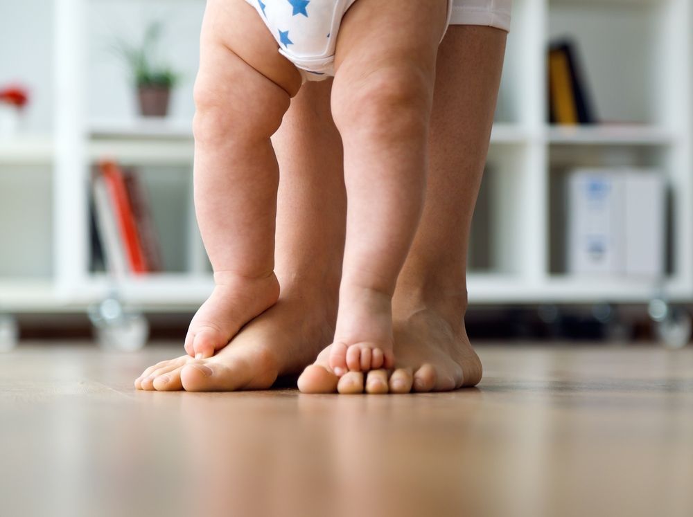 A Baby in a Diaper is Standing on a Wooden Floor — Craig Hughes Podiatry In Mount Hutton, NSW