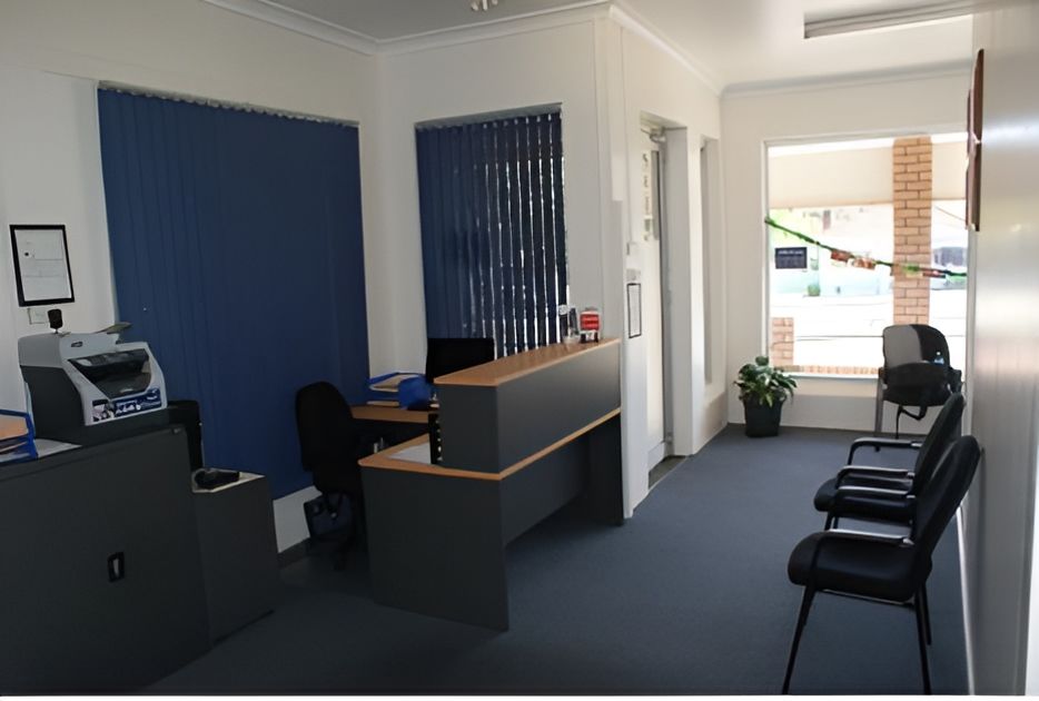 A Waiting Room With a Desk, Chairs and a Printer — Craig Hughes Podiatry in Mount Hutton, NSW