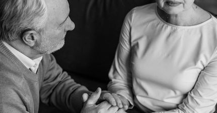 An elderly couple is sitting on a couch holding hands.