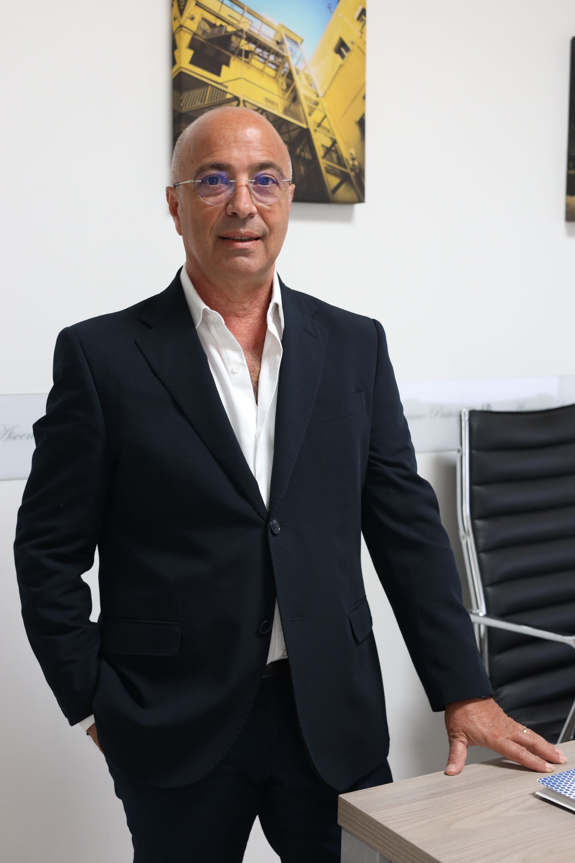 Un uomo in giacca e cravatta è in piedi davanti a una scrivania con le mani in tasca.