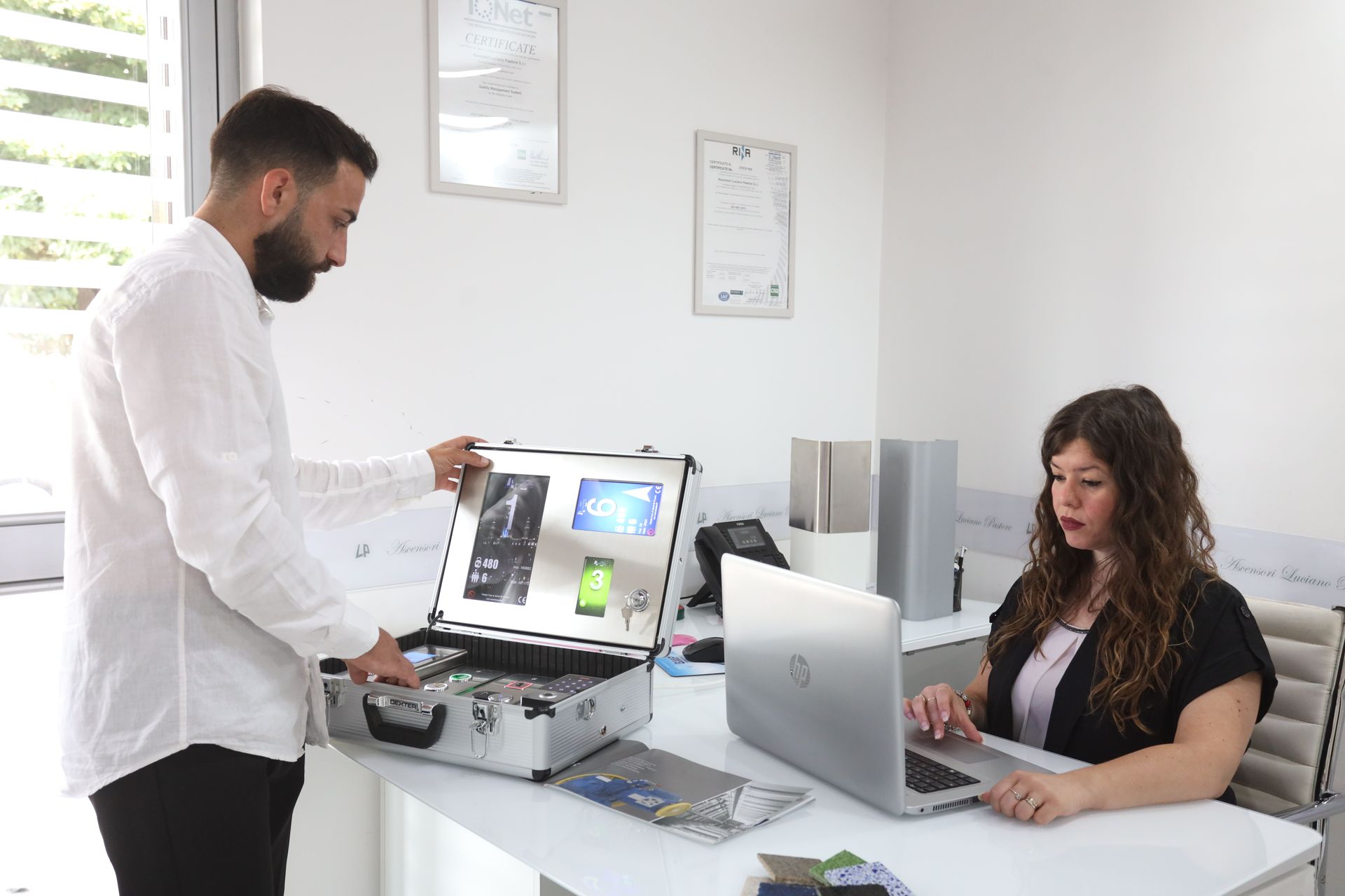 Un uomo è in piedi accanto a una donna seduta alla scrivania con un laptop.