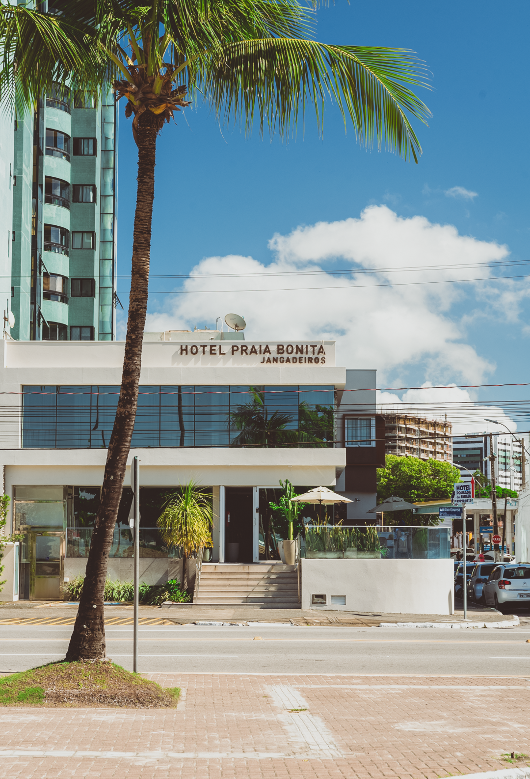 Hotel Praia Bonita com palmeiras, prédio azul claro e um céu azul brilhante.
