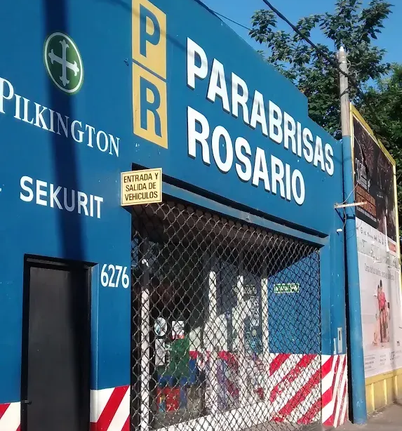Fachada azul de “Parabrisas Rosario” con letreros de Pilkington y Sekurit, puerta de metal y entrada.