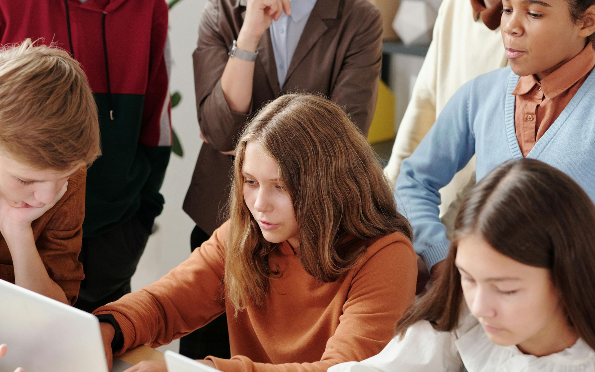 Students and an adult looking at a laptop together; a collaborative learning setting.