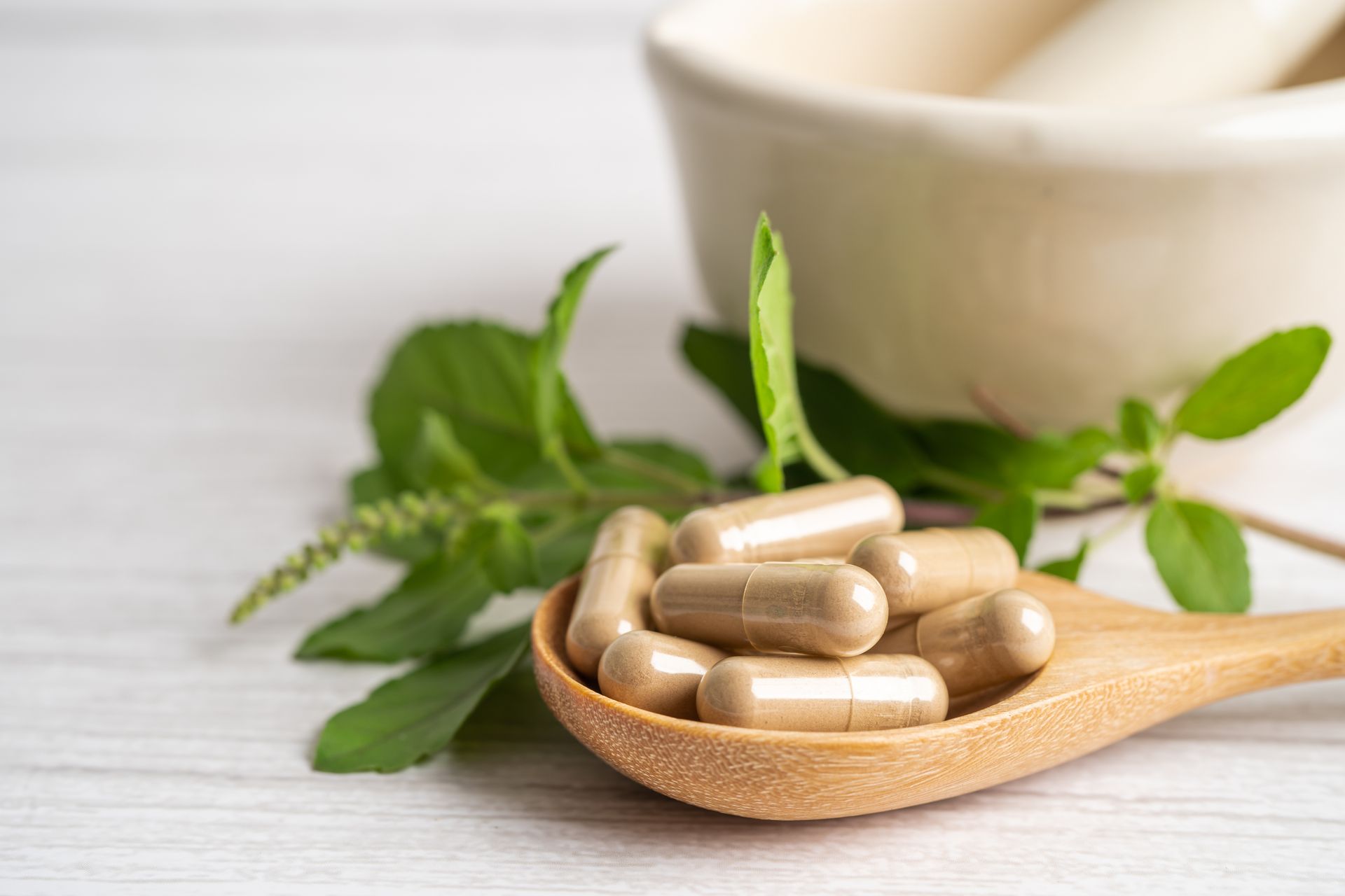 A wooden spoon filled with capsules next to a mortar and pestle.