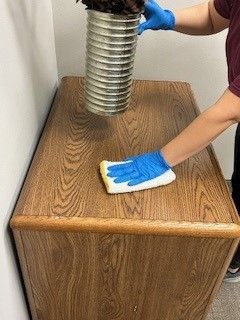 A person wearing blue gloves is cleaning a wooden table with a cloth.