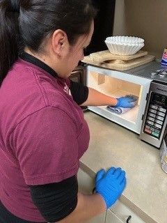 A woman is cleaning a microwave with a cloth and gloves.