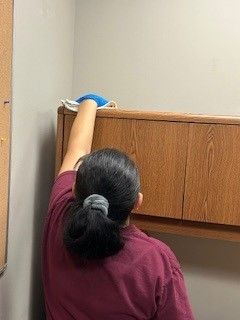 A woman is cleaning a wooden cabinet in a room.
