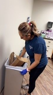 A woman is putting a cardboard box in a trash can.