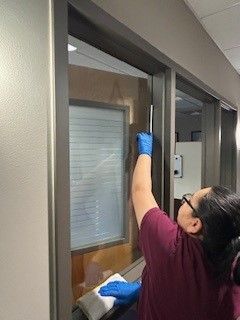 A woman is cleaning a window with a cloth in an office.