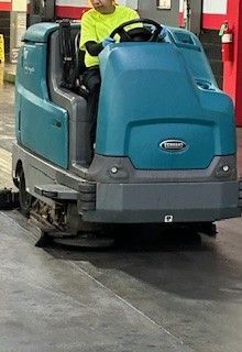 A man is driving a cleaning machine on a concrete floor.
