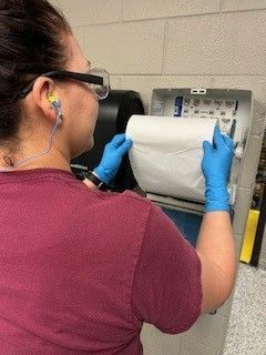 A woman wearing blue gloves is taking a roll of toilet paper out of a dispenser.