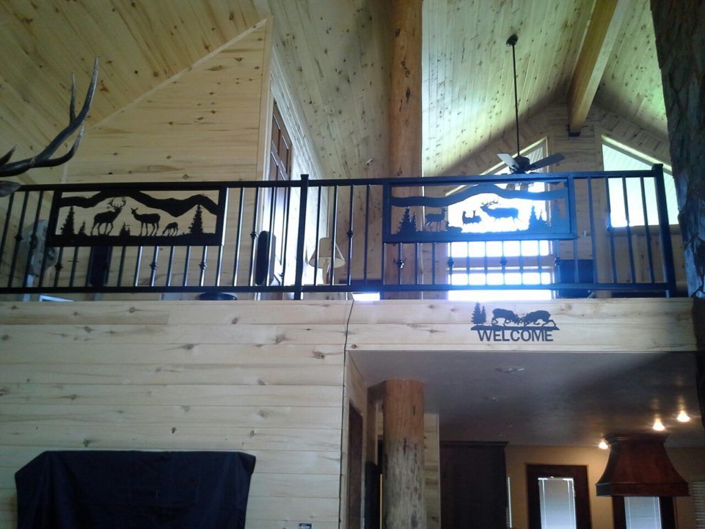 Black metal railing with wildlife cutouts in a rustic cabin, against light wood walls.
