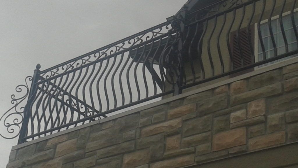 Black wrought iron balcony railing on a stone building exterior, overcast sky.