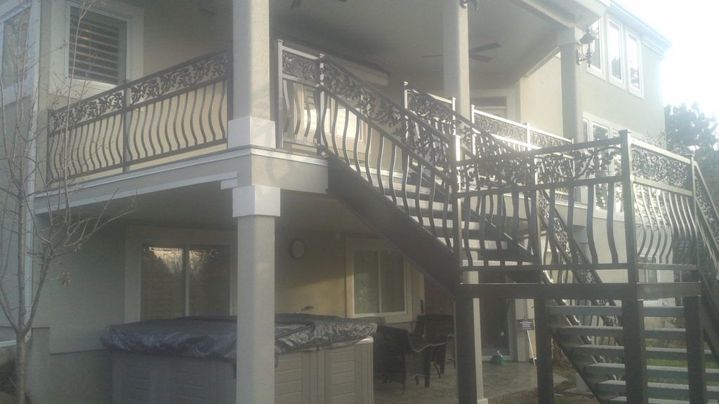 Backyard deck with dark metal railings and staircase leading down to the ground level.