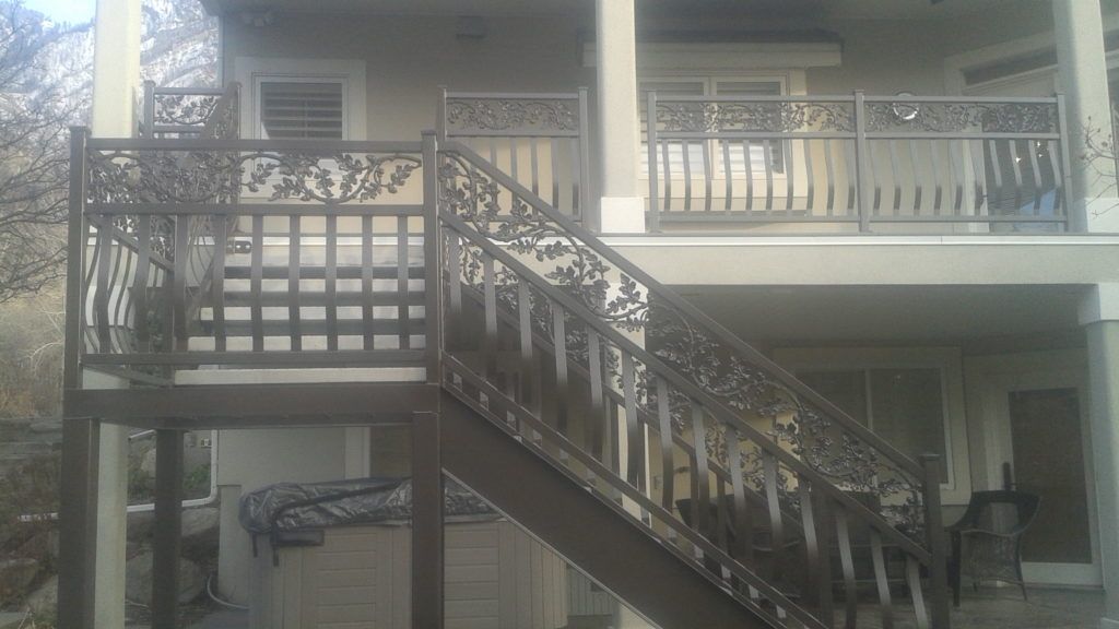 Brown deck with decorative metal railings and stairs leading to a second-story balcony.