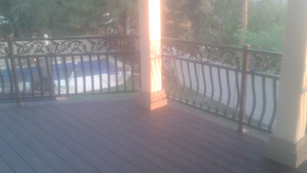 Deck with black metal railing overlooking a pool, trees in background, and wooden support columns.