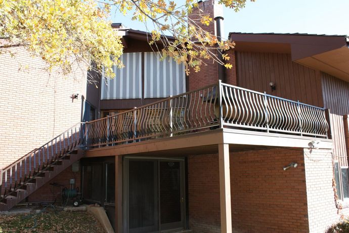 Exterior view of a two-story brick building with a wooden deck and staircase, featuring decorative metal railings.