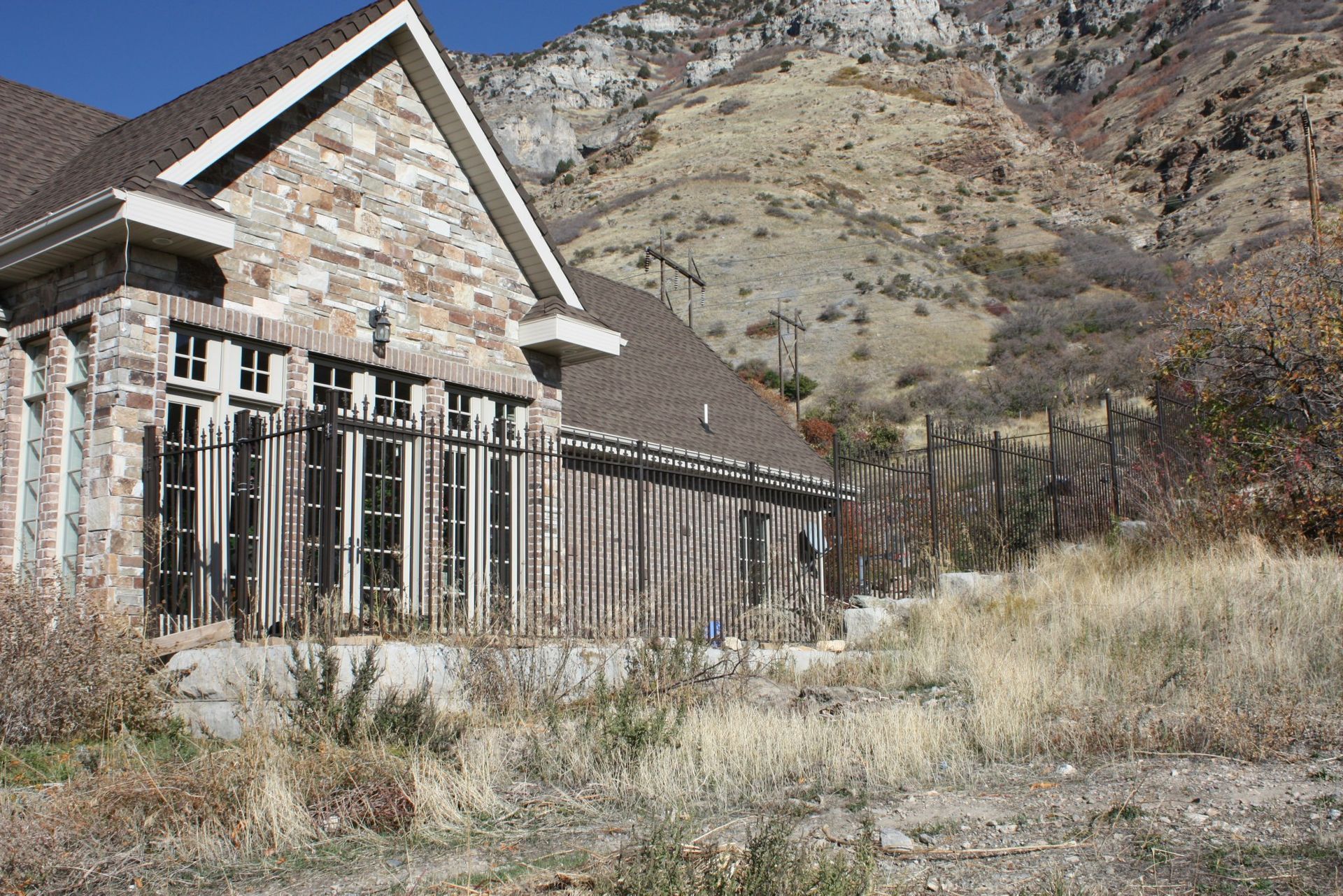 Stone house with dark trim and a brown roof, set against a dry hillside with sparse vegetation.
