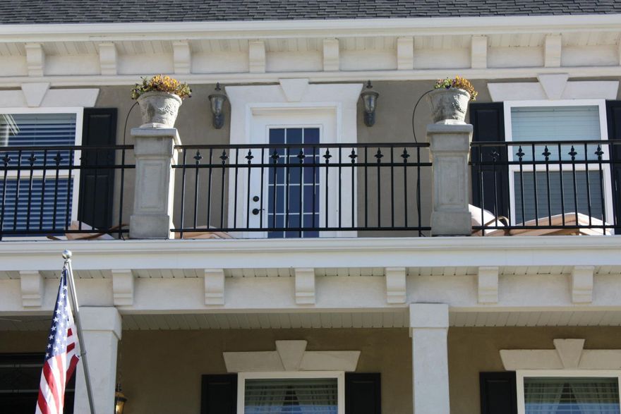 Balcony with black railing, white door, and potted plants; American flag in front.