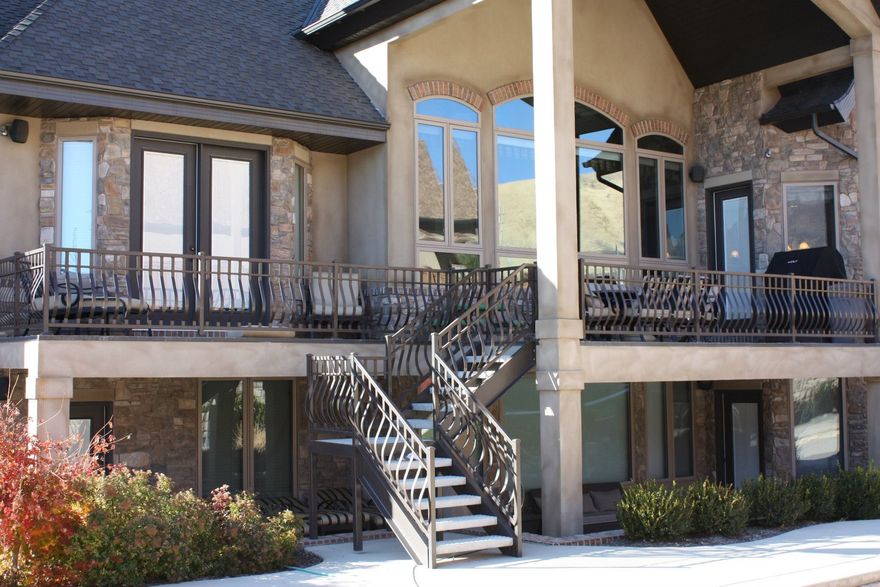 Two-story home with stone facade, multiple balconies with dark metal railings, and a central staircase leading up.