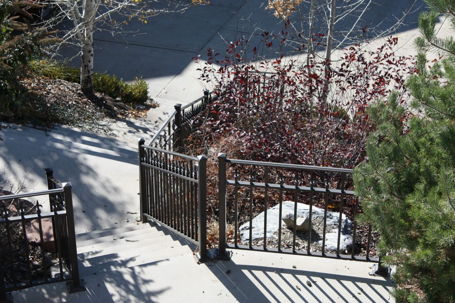 Metal railing on concrete steps leading towards a driveway and foliage.