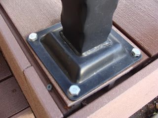 Black metal post base bolted to a brown composite deck.