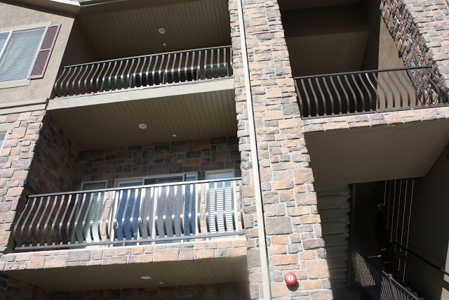 Multi-story building with stone facade and balconies with wavy metal railings.