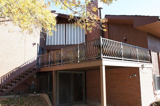 Brown and brick building with deck, metal railing, and staircase. Beige awning and sliding glass doors.