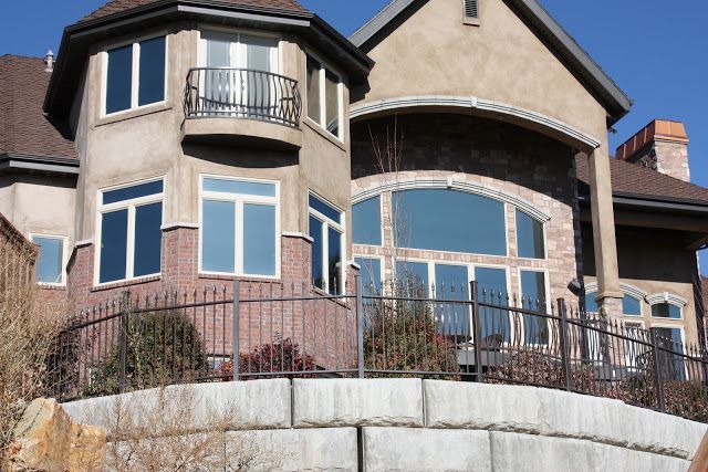 Tan stucco and brick house with large windows, balcony, and brown roof.