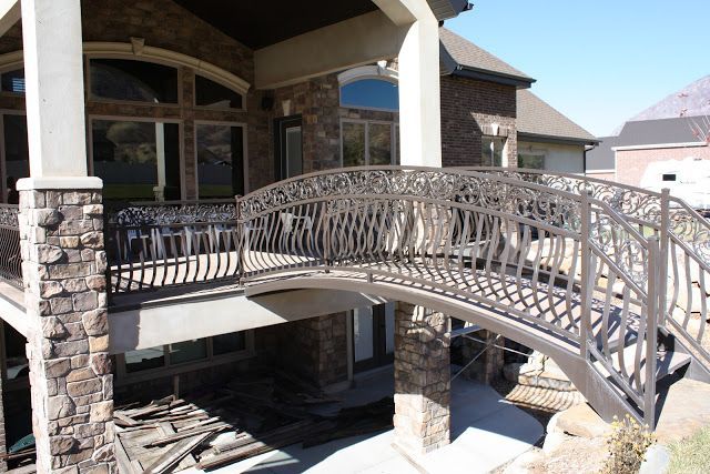 A decorative arched metal bridge connects two levels of a house with stone pillars and brown brick.