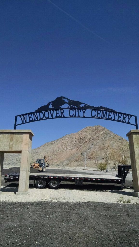 Entrance to Wendover City Cemetery under blue sky; a flatbed trailer is parked below.