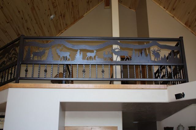 Metal railing with wildlife silhouette design, overlooking interior. Brown wood ceiling and beige walls.