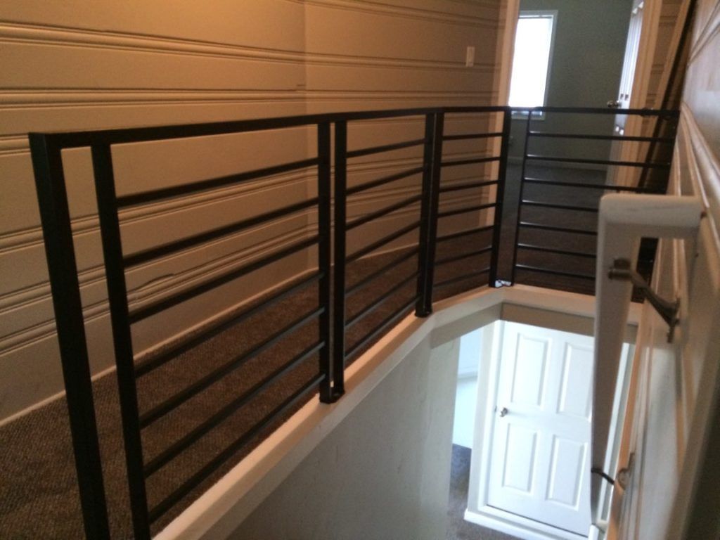Black metal railing along a hallway overlooking a stairwell with a white door.