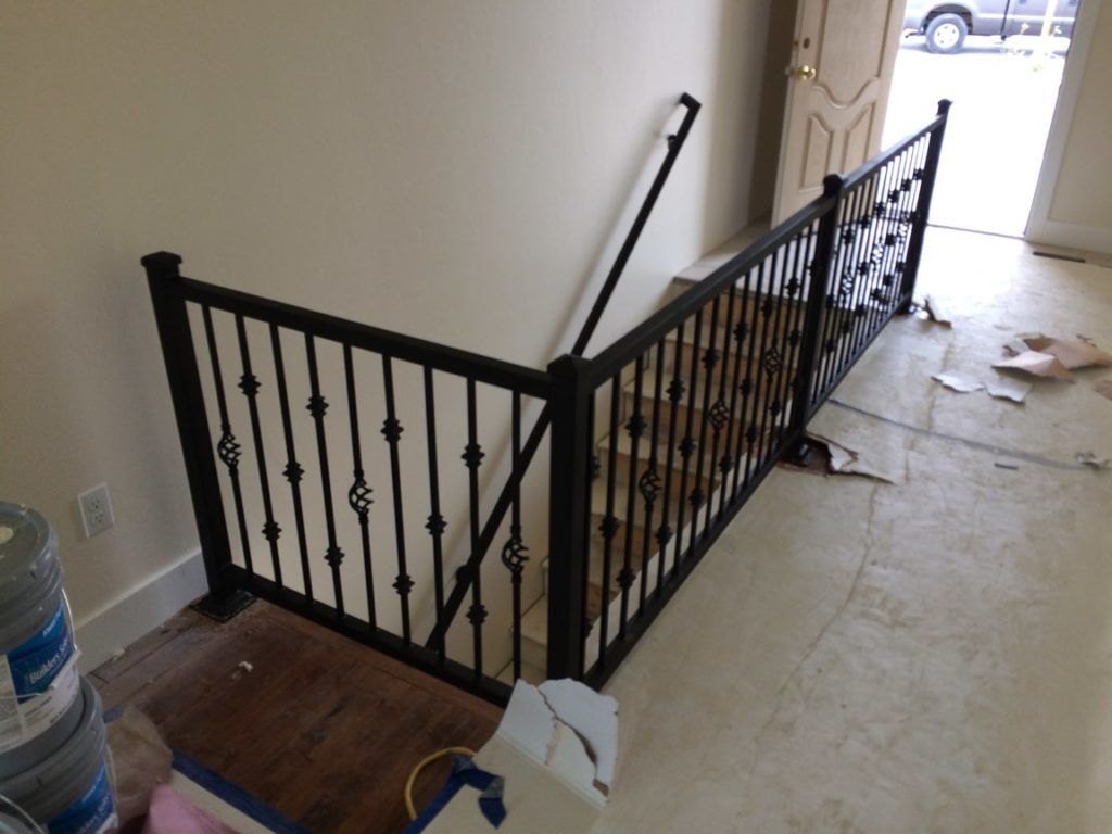 Black metal railing along a staircase. Brown wooden steps are visible. Beige walls and unfinished flooring.