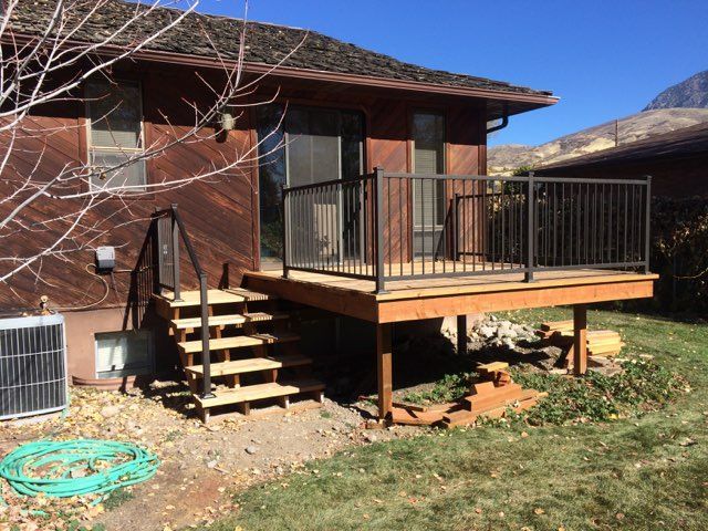 Wooden deck with stairs attached to a brown house with a metal railing, blue sky.
