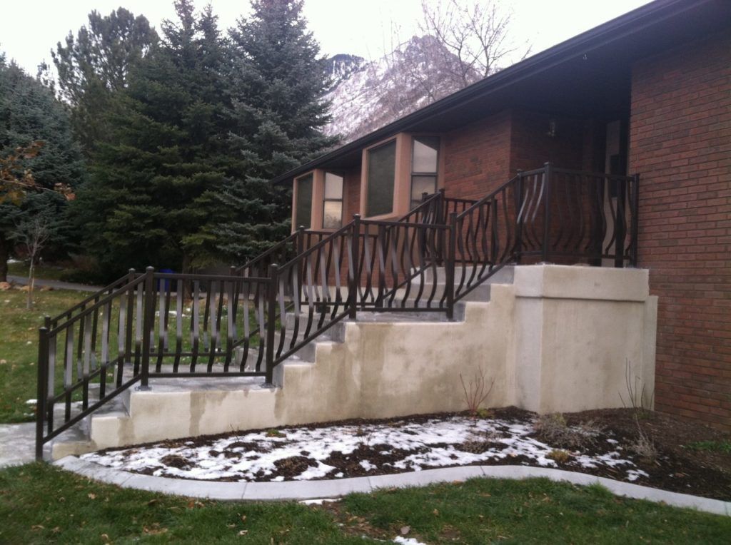 Brick house with concrete steps and black metal railings, snow on the ground.