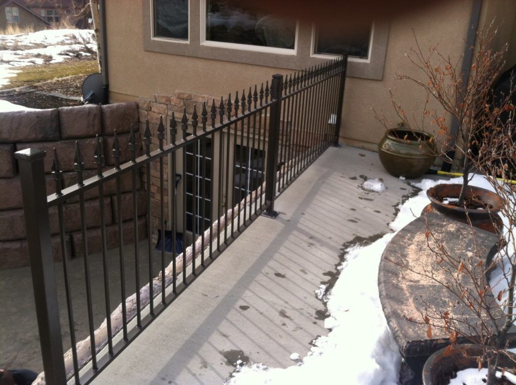 Black metal fence around a concrete sunken patio area with snow patches and a retaining wall.
