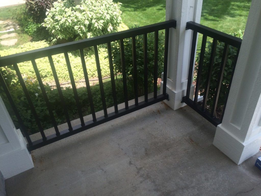 Black railing on a concrete porch, with green bushes in the background.
