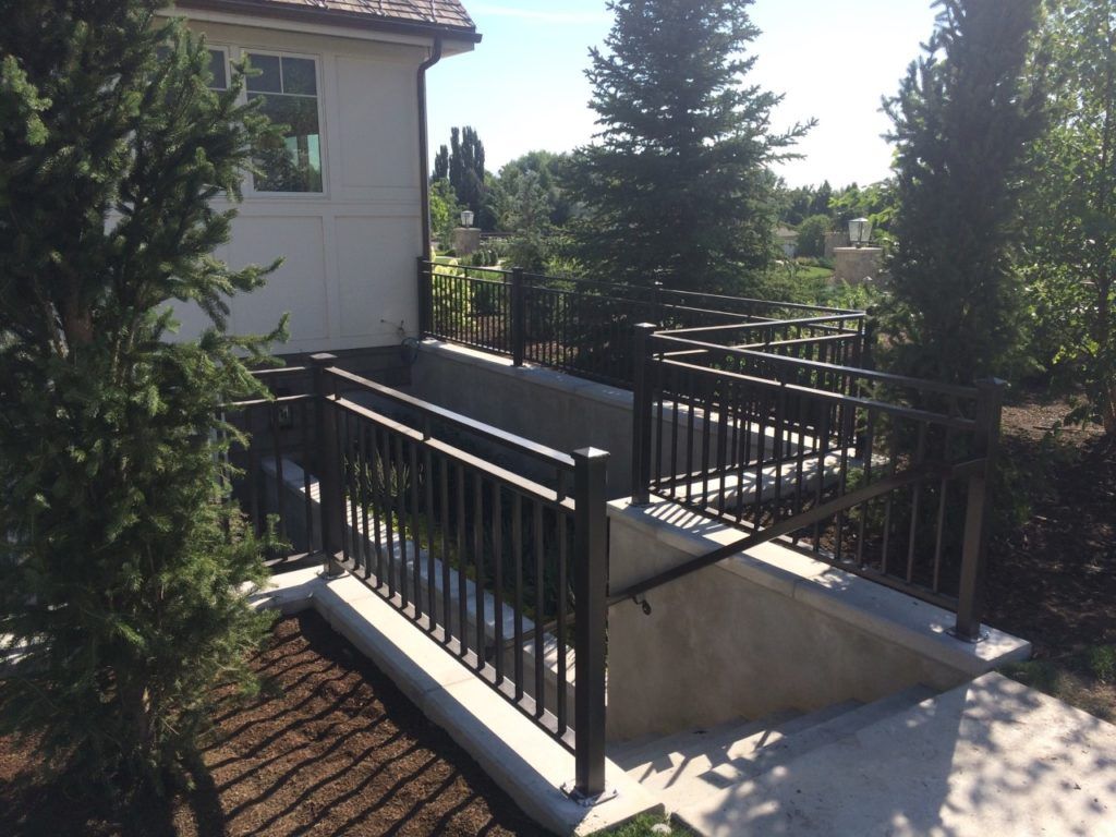 Concrete ramp and stairs with black metal railings leading down to a building entrance.