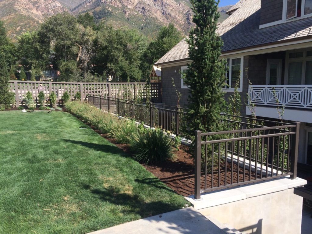 Backyard with green grass, landscaping bed, brown fence, and a house with mountains in the background.