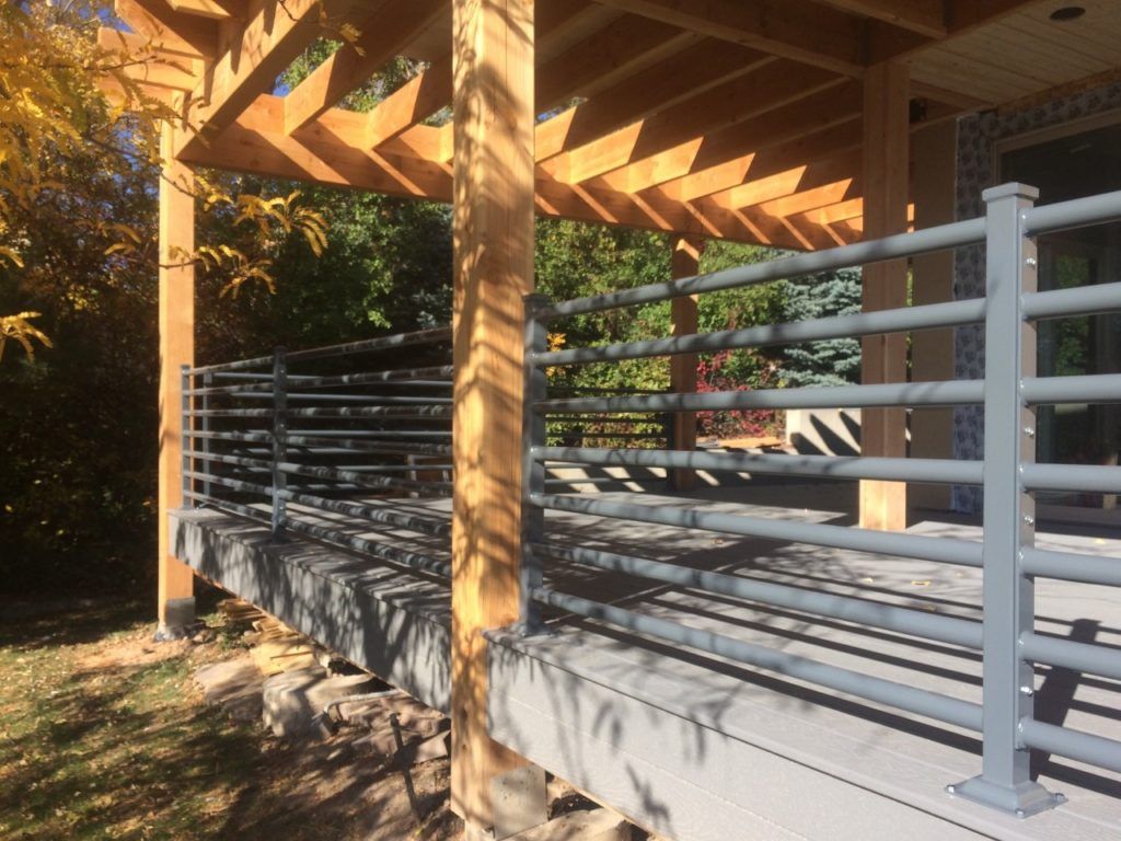 Gray deck railing under a wooden pergola on a sunny day.